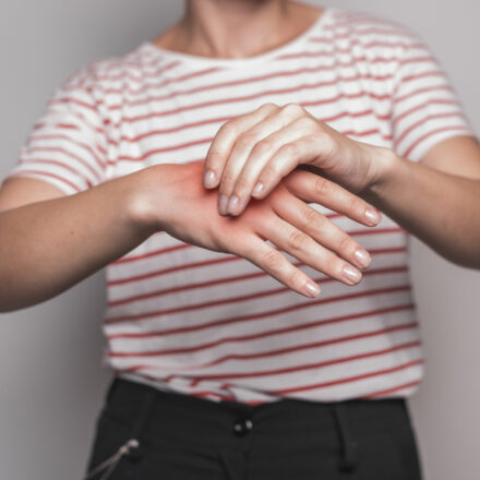 Mid section young woman having pain hand against gray background